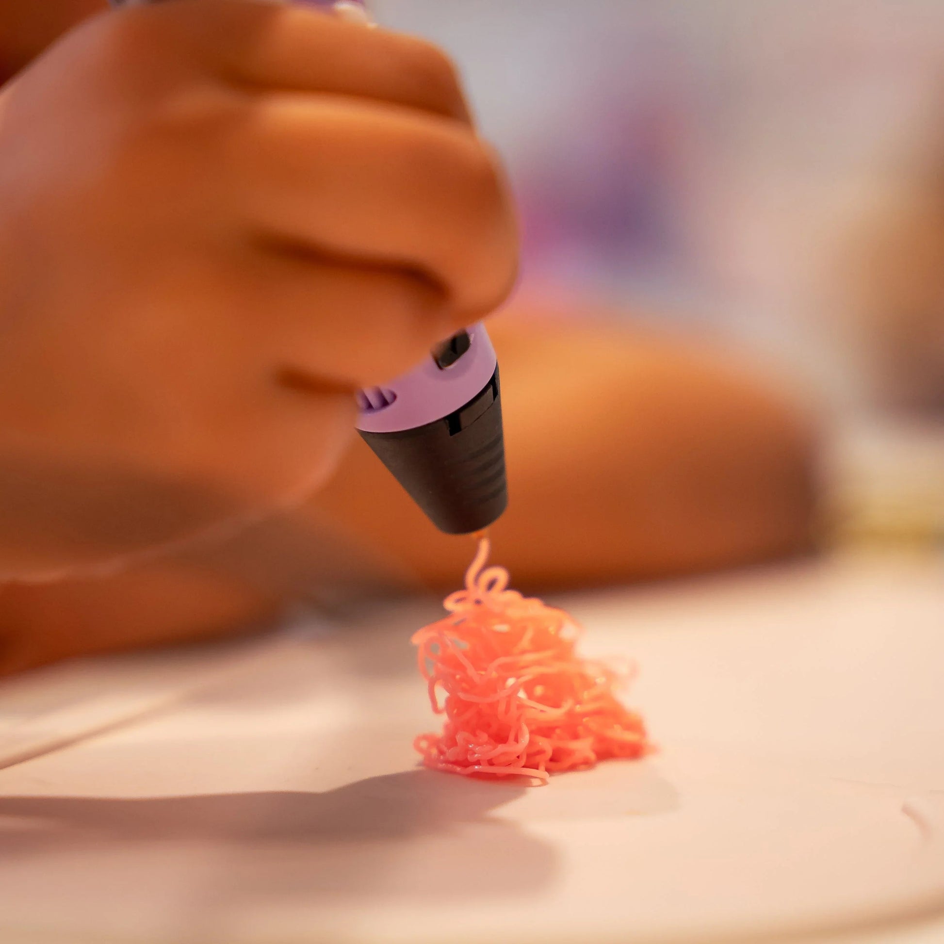 Barn hånd bruger lilla 3D-pen til at tegne med pink plast på hvidt bord.
