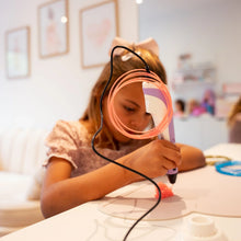 Barn bruger 3D pen til kreativt projekt ved bord, orange filament synligt