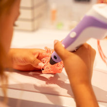 Barn bruger lilla 3D pen til at tegne kreative former på bordet